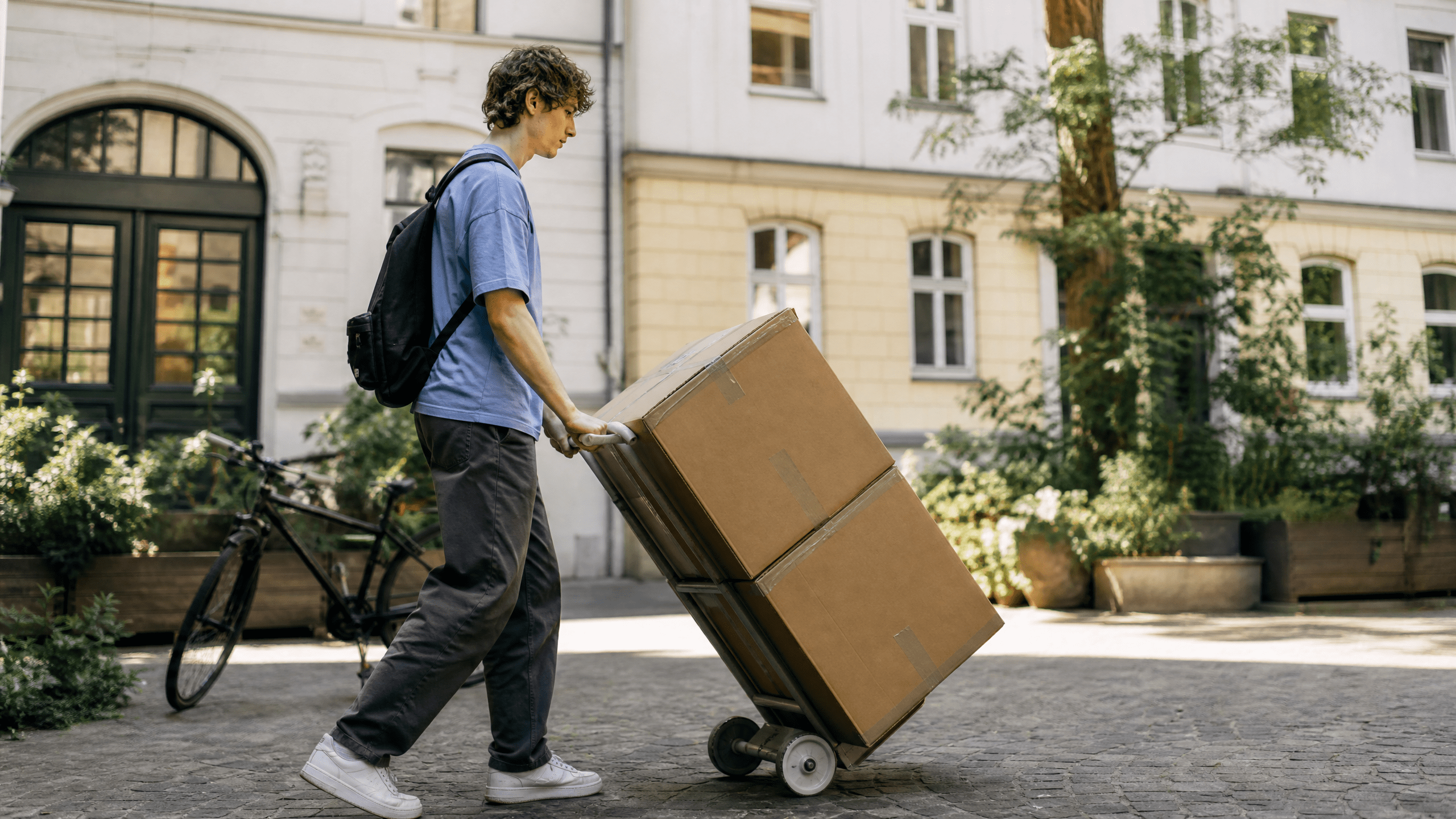 Student transportiert wenige Umzugskartons mit einem kleinen Handtrolley durch einen Berliner Innenhof.