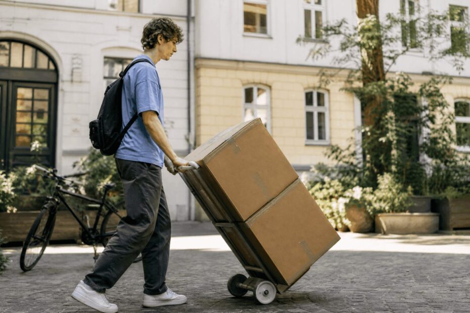 Fahrrad Umzug – junger Mann schiebt Kartons auf einer Sackkarre